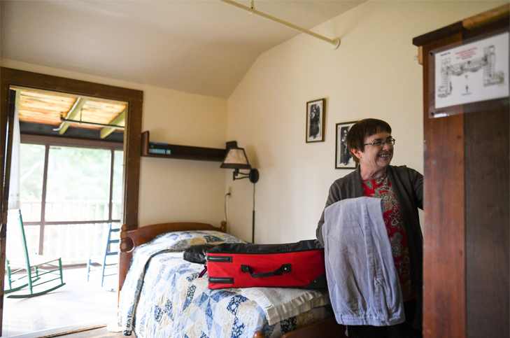 An Adelynrood guest unpacks in a cozy room that opens to a porch with rocking chairs.